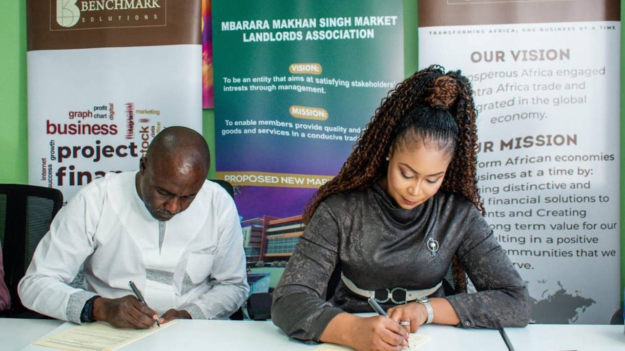 A male (left) and female (female) executive, both seated, signing a funding agreement between their two companies
