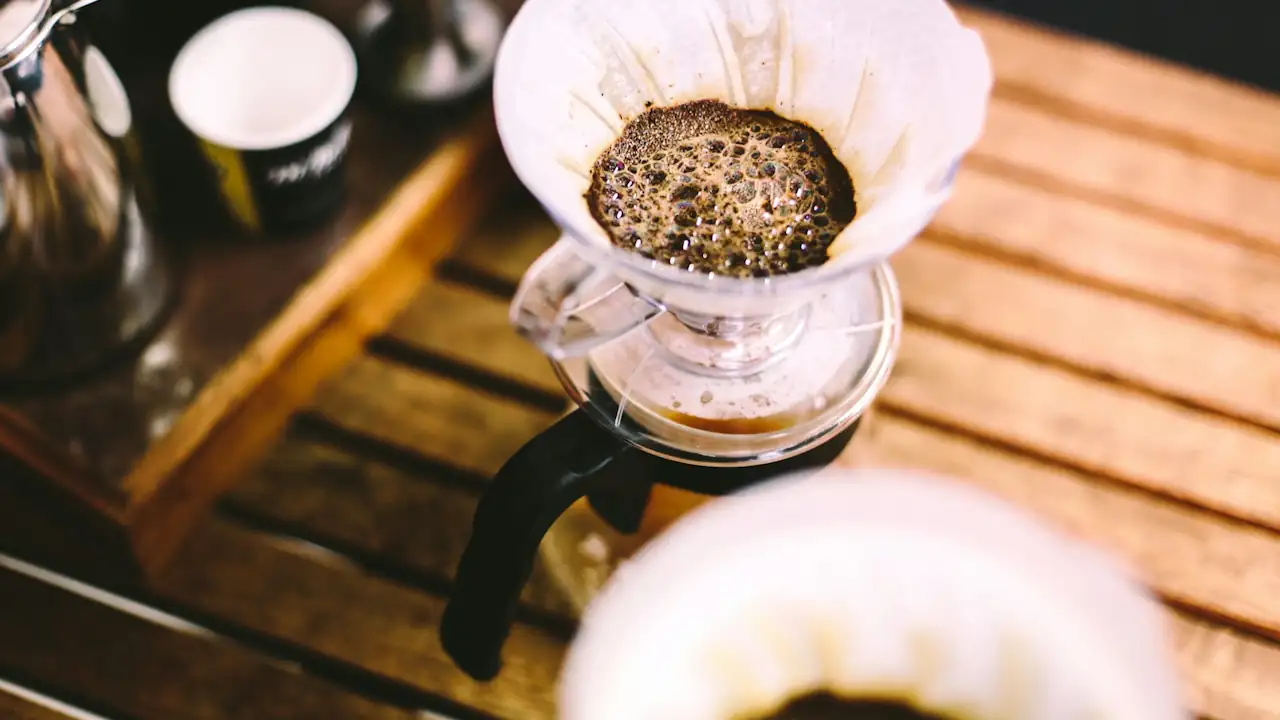 A detailed shot of the coffee brewing process, showing golden-brown bubbles forming on saturated grounds in a manual pour-over dripper.