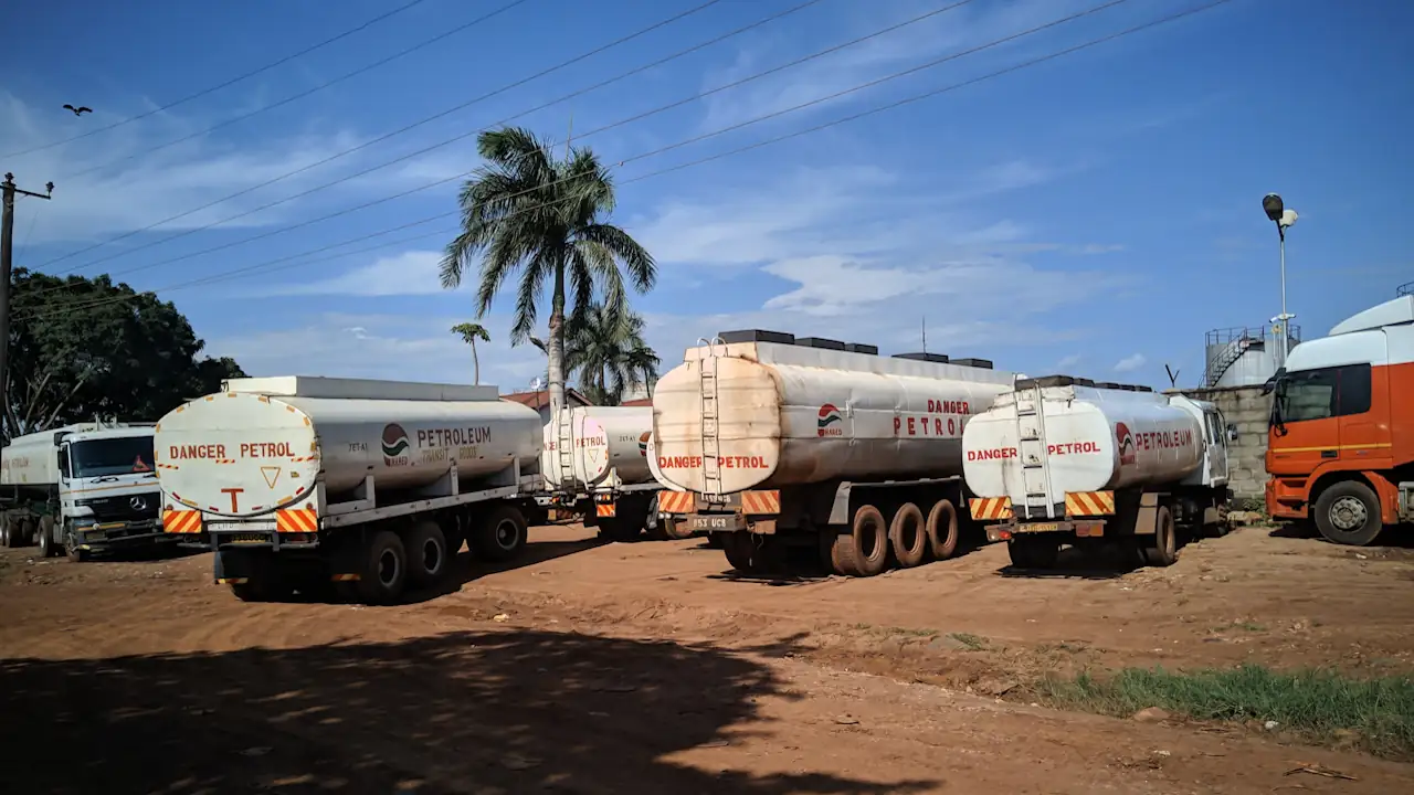 Several white fuel tankers bearing "Danger Petrol" signs parked on a dirt lot at a storage depot in Jinja, Uganda, under a blue sky.