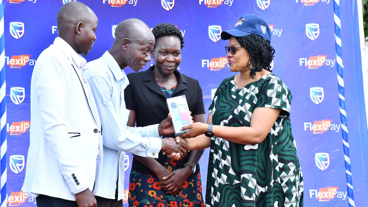 Irene Muwanguzi, the Parish Development Model's Deputy Director for Enterprise Development, hands over a phone to a beneficiary SACCO member