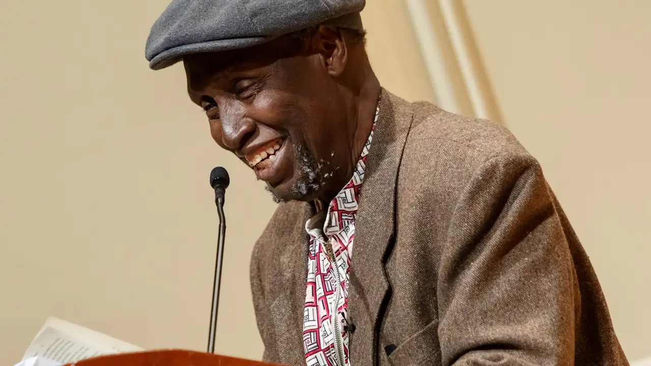 An elderly man smilles while he stands reading at a dais