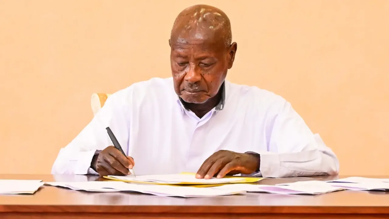 Medium shot of Ugandan President Yoweri Museveni signing an official act into law at State House.