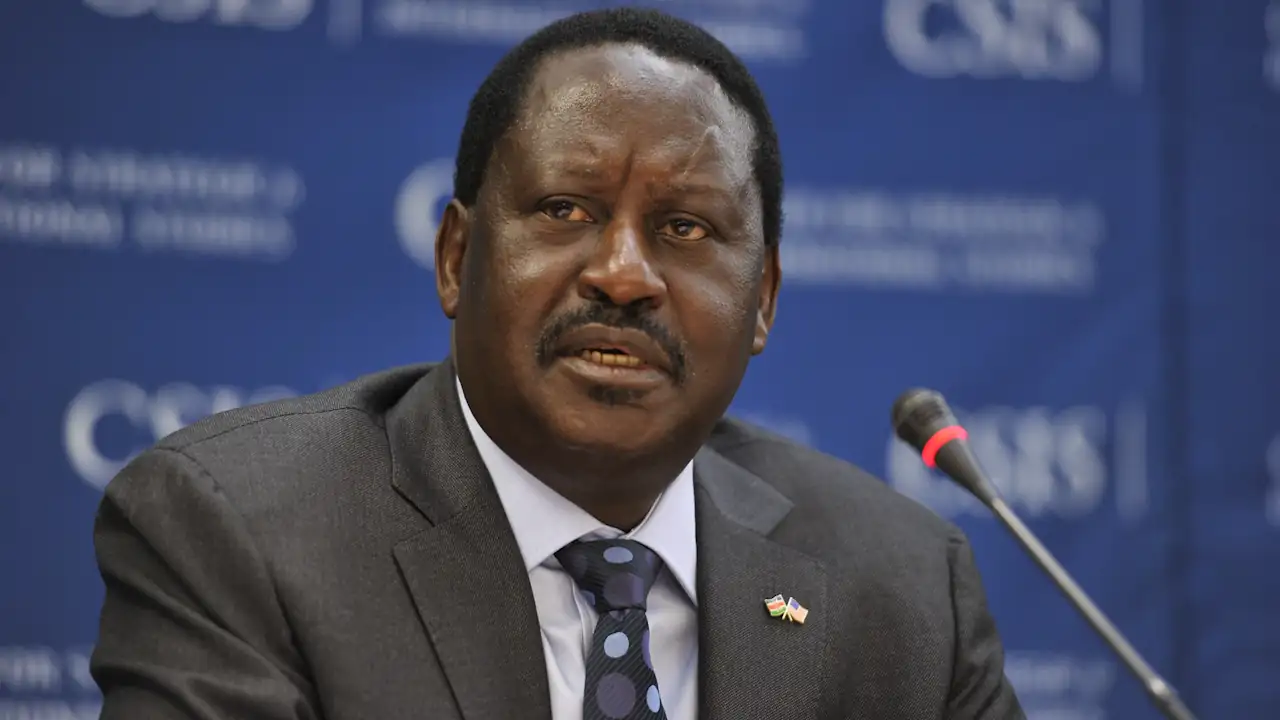 A man seated at a conference table delivers a speech. The camera is focussed on his face, while his background is mainly blurred. He is facing away from the partially blurred microphone and looking at someone in the audience. The man, Raila Odinga, passed away in India on 15 October 2025.