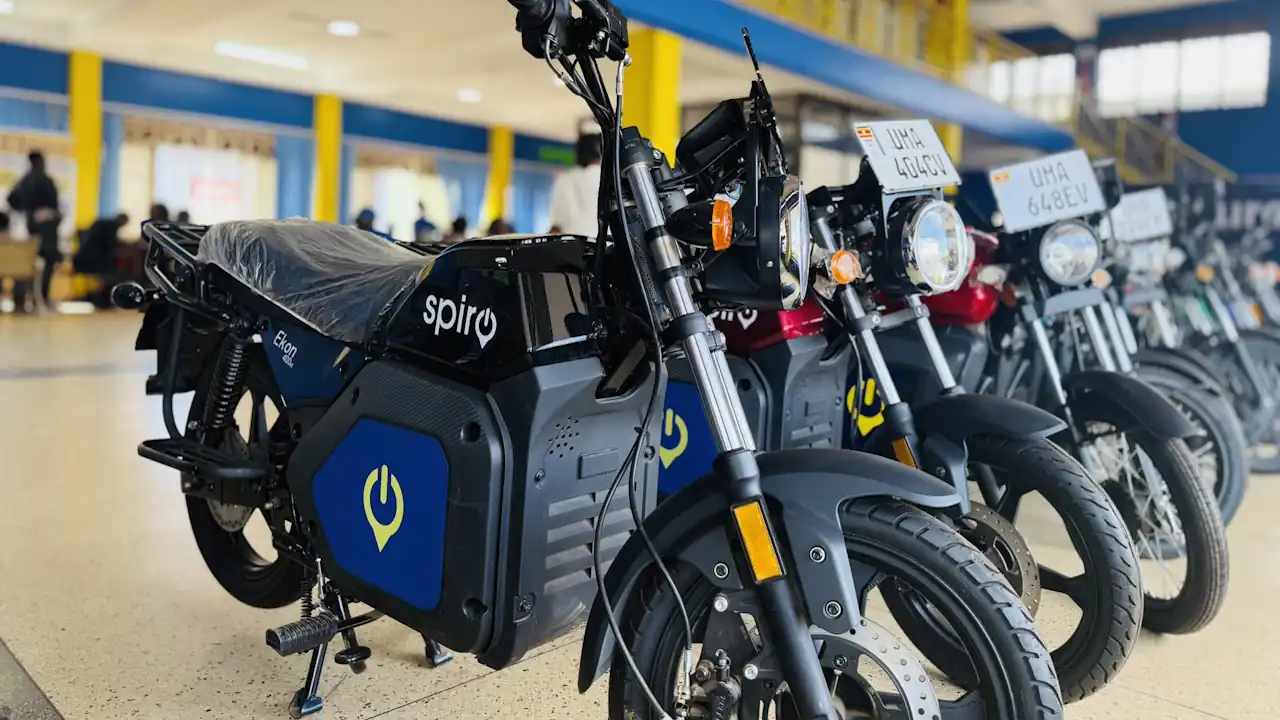 Row of black electric motorcycles with blue side panels and the Spiro logo, parked side by side in a large indoor hall