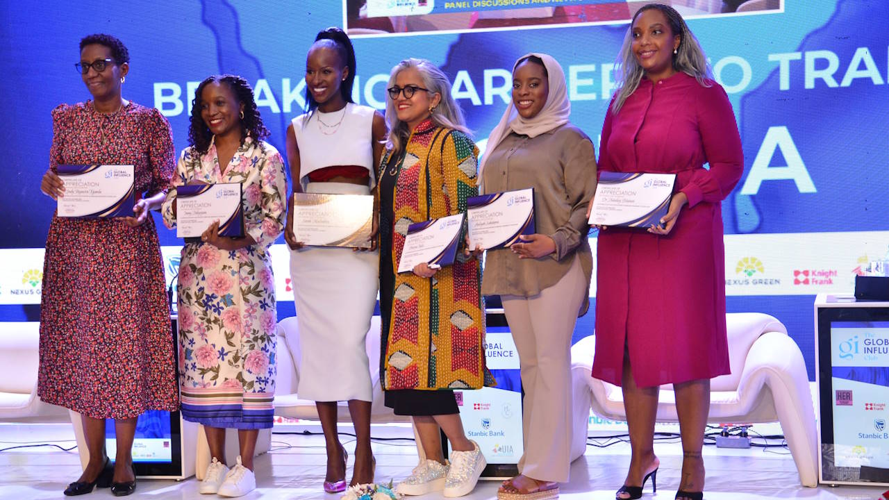 A row of five women, each holding certificates on a stage at a formal event