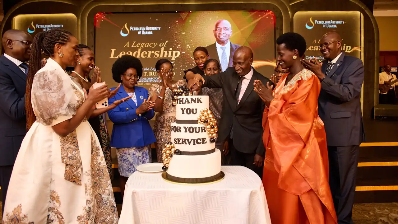 Ernest Rubondo cuts a three-tier cake reading "Thank You For Your Service" on a stage lit for "A Legacy of Leadership," surrounded by applauding guests including a woman in a blue jacket.