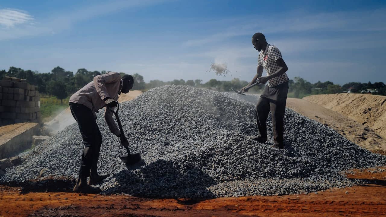 Two men shovelling gravel on a construction site